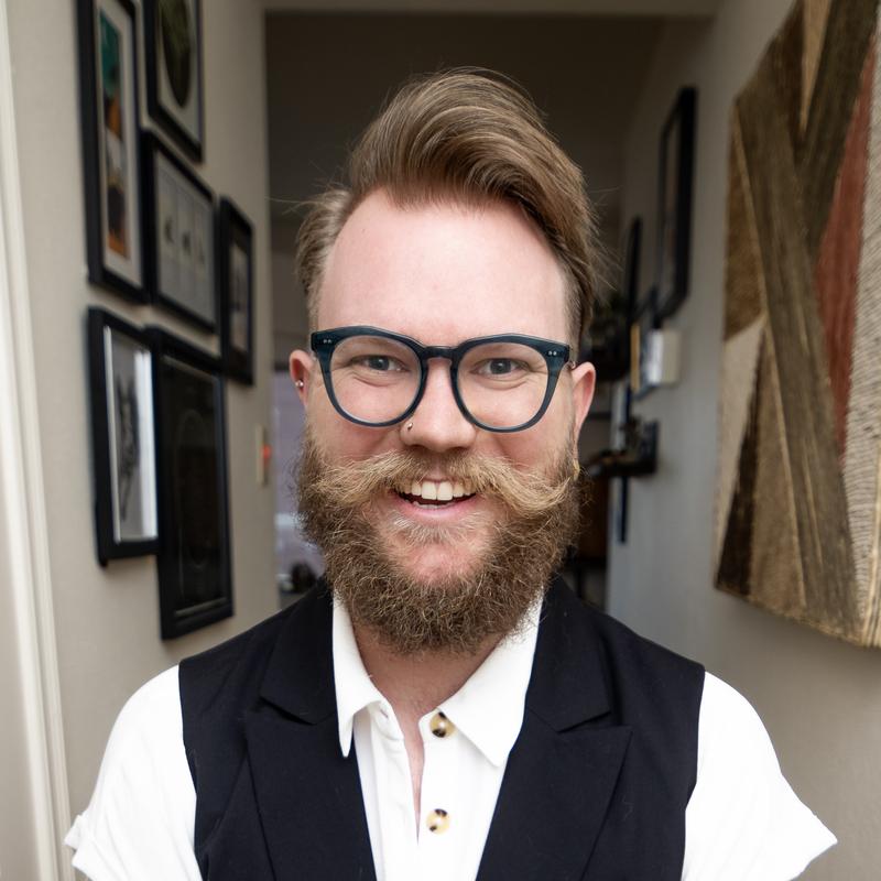 Portrait of Geoffrey wearing dark glasses, vest, shirt, and tie.
